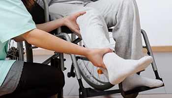 Healthcare worker supports the bandaged foot of a patient seated in a wheelchair.